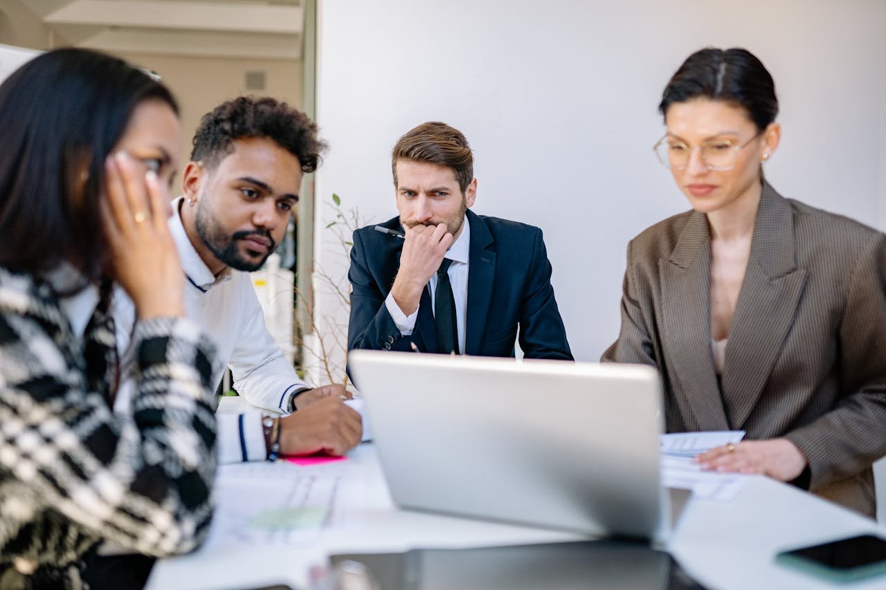 Focused team of professionals discussing work at a laptop during an office meeting.